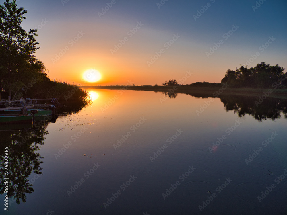 Quiet morning on the river. The sun rises over the horizon. Trees, boats stand in silence.