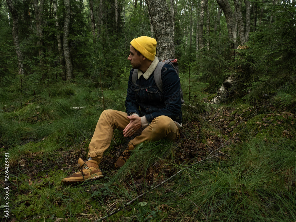 Young stylish hipster sits in woods or forest having rest and looking 