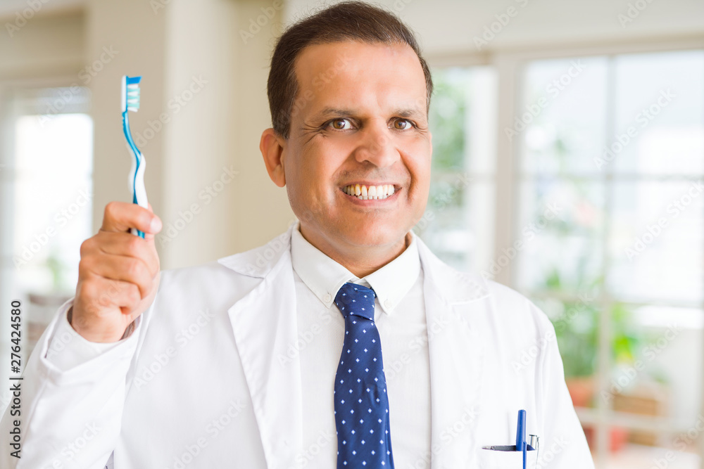 Middle age dentist man holding toothbrush and smiling Middle age dentist man holding toothbrush and smiling
