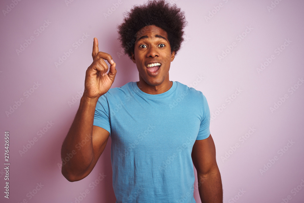 African american man with afro hair wearing blue t-shirt standing over isolated pink background pointing finger up with successful idea. Exited and happy. Number one. African american man with afro hair wearing blue t-shirt standing over isolated pink background pointing finger up with successful idea. Exited and happy. Number one.