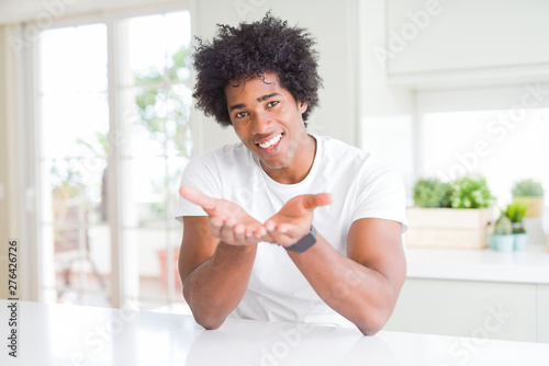 Young african american man wearing casual white t-shirt sitting at home Smiling with hands palms together receiving or giving gesture. Hold and protection