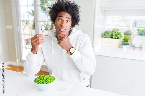 African American man eating fresh green peas at home serious face thinking about question  very confused idea