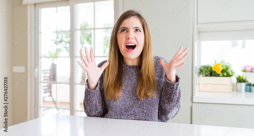 Beautiful young woman at home crazy and mad shouting and yelling with aggressive expression and arms raised. Frustration concept. Beautiful young woman at home crazy and mad shouting and yelling with aggressive expression and arms raised. Frustration concept.