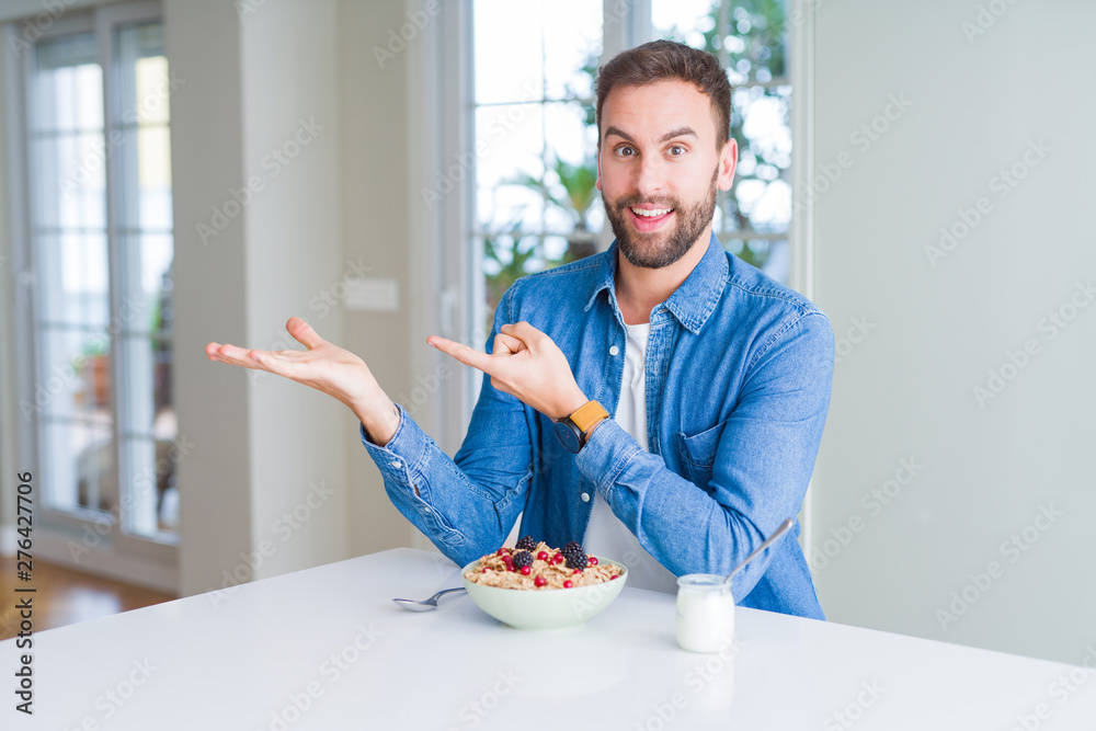 Handsome man eating cereals for breakfast at home amazed and smiling to the camera while presenting with hand and pointing with finger. Handsome man eating cereals for breakfast at home amazed and smiling to the camera while presenting with hand and pointing with finger.