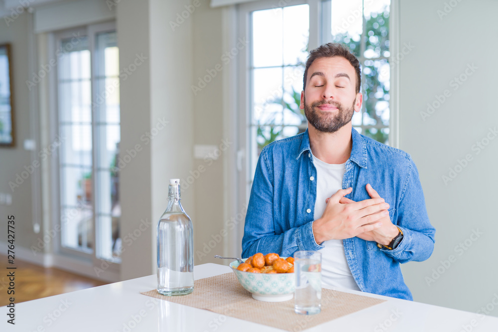 Handsome man eating pasta with meatballs and tomato sauce at home smiling with hands on chest with closed eyes and grateful gesture on face. Health concept. Handsome man eating pasta with meatballs and tomato sauce at home smiling with hands on chest with closed eyes and grateful gesture on face. Health concept.