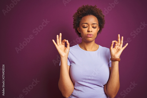 Young beautiful african american woman with afro hair over isolated purple background relax and smiling with eyes closed doing meditation gesture with fingers. Yoga concept.