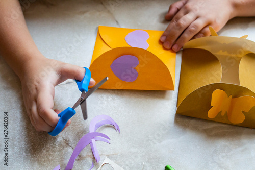 Crafts for children. The child makes a colorful paper craft. postcard. The child does crafts. Creative little boy with envelopes and scissors.