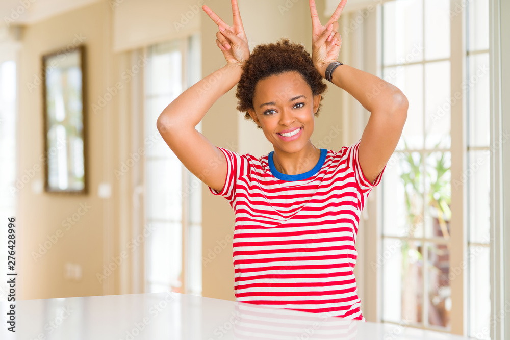 Young beautiful african american woman at home Posing funny and crazy with fingers on head as bunny ears, smiling cheerful Young beautiful african american woman at home Posing funny and crazy with fingers on head as bunny ears, smiling cheerful