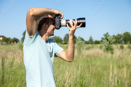 young male photographer in nature with a big professional camera on a sunny summer day