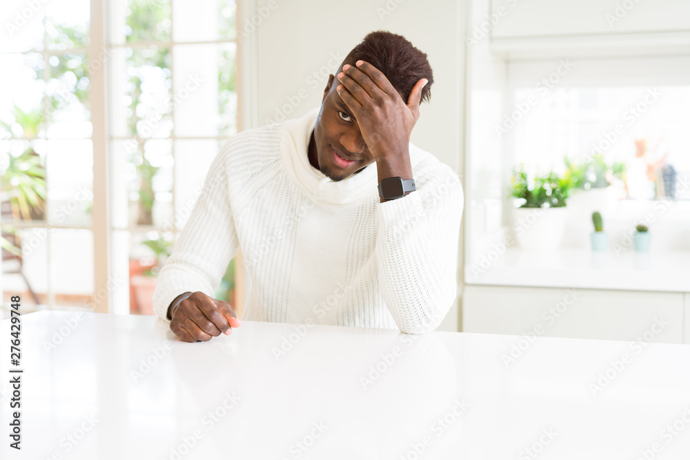 Handsome african american man on white table surprised with hand on head for mistake, remember error. Forgot, bad memory concept.