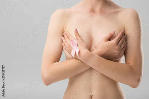 partial view of topless young woman with pink ribbon covering breast isolated on grey