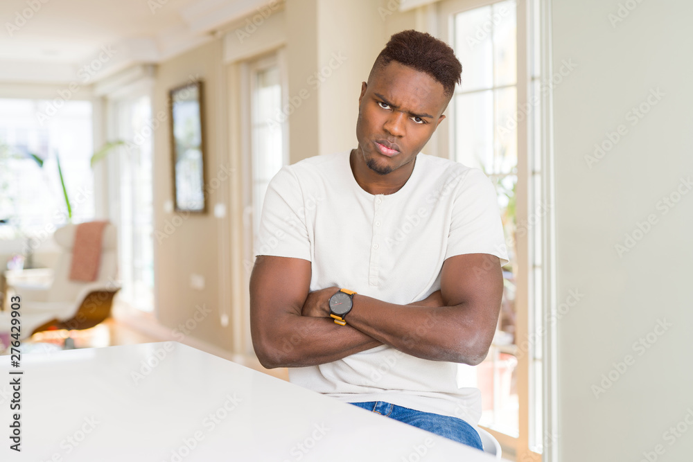 Handsome african american man on white table at home skeptic and nervous, disapproving expression on face with crossed arms. Negative person.