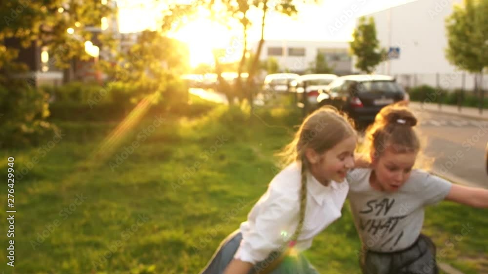 Happy childhood. Two girls schoolgirls laughing in the rays of the setting sun. One girl falls, school holidays Happy childhood. Two girls schoolgirls laughing in the rays of the setting sun. One girl falls, school holidays