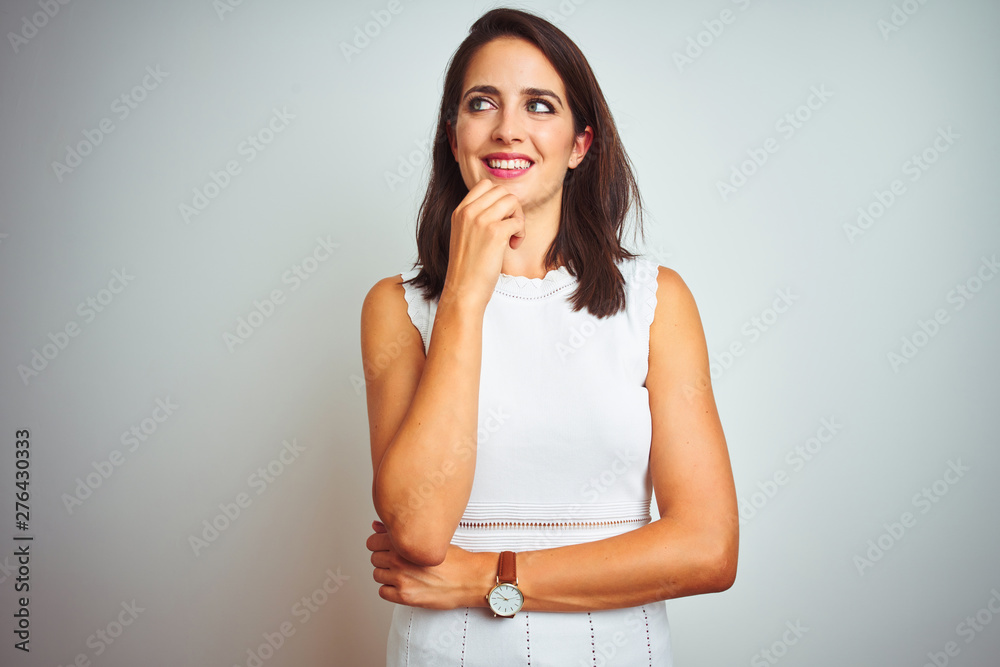 Young beautiful woman wearing dress standing over white isolated background with hand on chin thinking about question, pensive expression. Smiling and thoughtful face. Doubt concept. Young beautiful woman wearing dress standing over white isolated background with hand on chin thinking about question, pensive expression. Smiling and thoughtful face. Doubt concept.