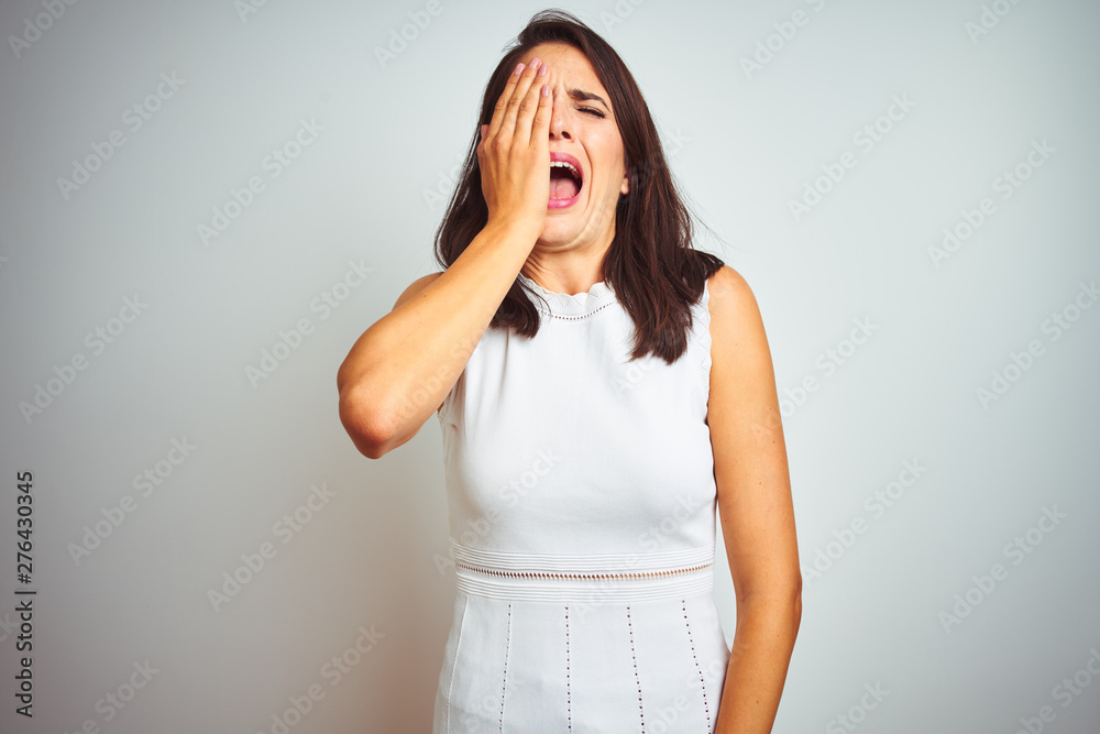 Young beautiful woman wearing dress standing over white isolated background Yawning tired covering half face, eye and mouth with hand. Face hurts in pain. Young beautiful woman wearing dress standing over white isolated background Yawning tired covering half face, eye and mouth with hand. Face hurts in pain.