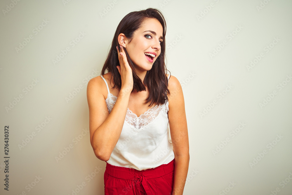 Young beautiful woman wearing t-shirt standing over white isolated background smiling with hand over ear listening an hearing to rumor or gossip. Deafness concept. Young beautiful woman wearing t-shirt standing over white isolated background smiling with hand over ear listening an hearing to rumor or gossip. Deafness concept.