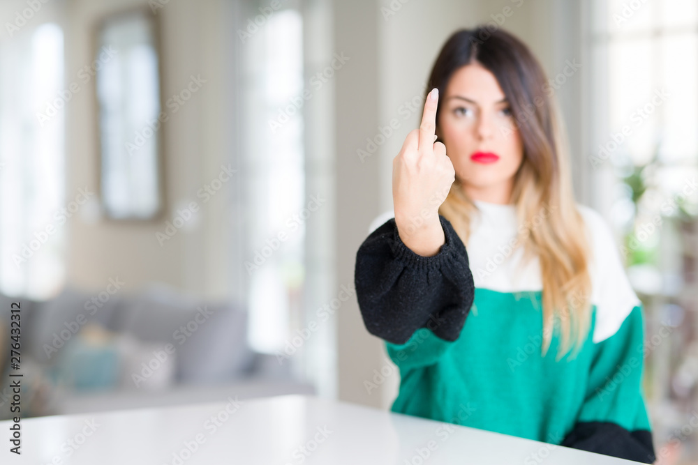 Young beautiful woman wearing winter sweater at home Showing middle finger, impolite and rude fuck off expression Young beautiful woman wearing winter sweater at home Showing middle finger, impolite and rude fuck off expression