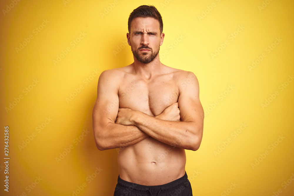Young handsome shirtless man over isolated yellow background skeptic and nervous, disapproving expression on face with crossed arms. Negative person.