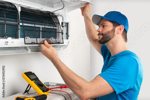 Installation service fix  repair maintenance of an air conditioner indoor unit, by cryogenist technican worker checking the air filter in blue shirt baseball cap