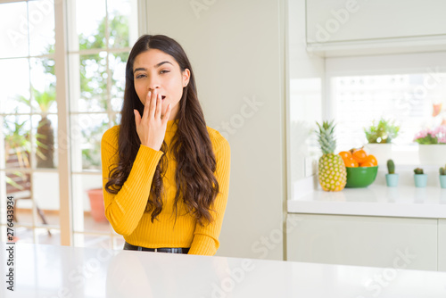 Young beautiful woman at home on white table bored yawning tired covering mouth with hand. Restless and sleepiness.