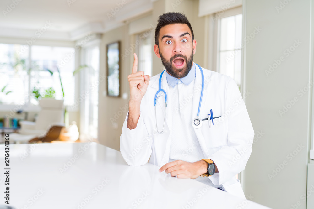 Handsome hispanic doctor man wearing stethoscope at the clinic pointing finger up with successful idea. Exited and happy. Number one. Handsome hispanic doctor man wearing stethoscope at the clinic pointing finger up with successful idea. Exited and happy. Number one.