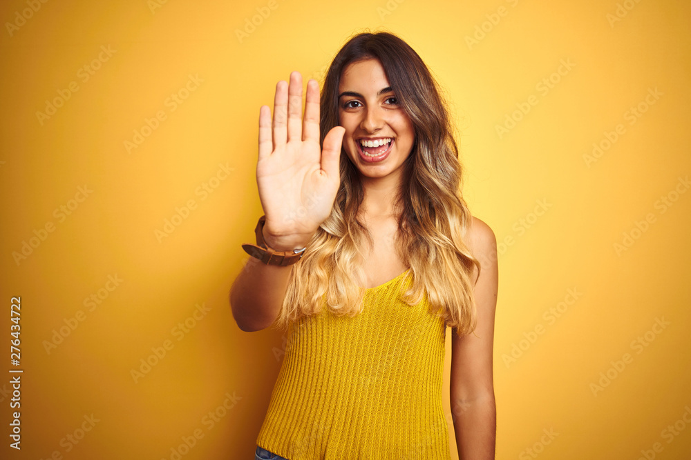 Young beautiful woman wearing t-shirt over yellow isolated background Waiving saying hello happy and smiling, friendly welcome gesture Young beautiful woman wearing t-shirt over yellow isolated background Waiving saying hello happy and smiling, friendly welcome gesture