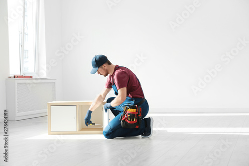 Handyman in uniform assembling furniture indoors, space for text. Professional construction tools © New Africa