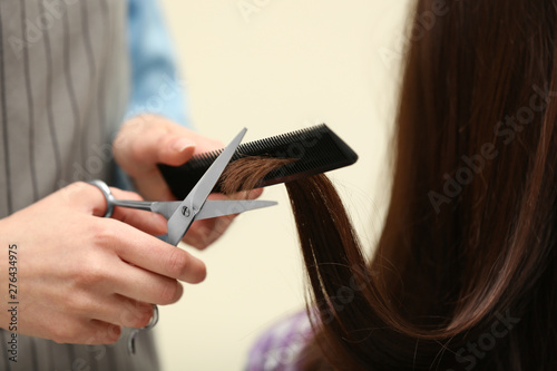 Barber making stylish haircut with professional scissors in beauty salon, closeup