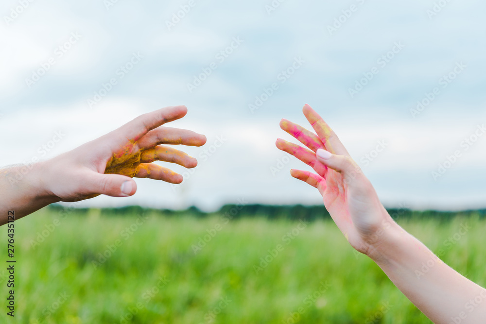 cropped view of man and woman with holi paint on hands gesturing near blue sky cropped view of man and woman with holi paint on hands gesturing near blue sky