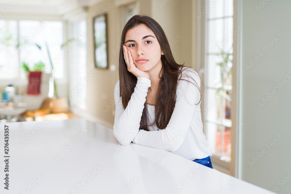 Beautiful young woman sitting on white table at home thinking looking tired and bored with depression problems with crossed arms. Beautiful young woman sitting on white table at home thinking looking tired and bored with depression problems with crossed arms.