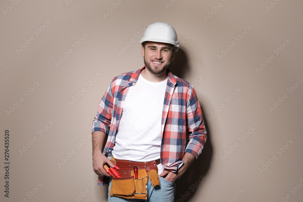 Young working man in hardhat standing on color background