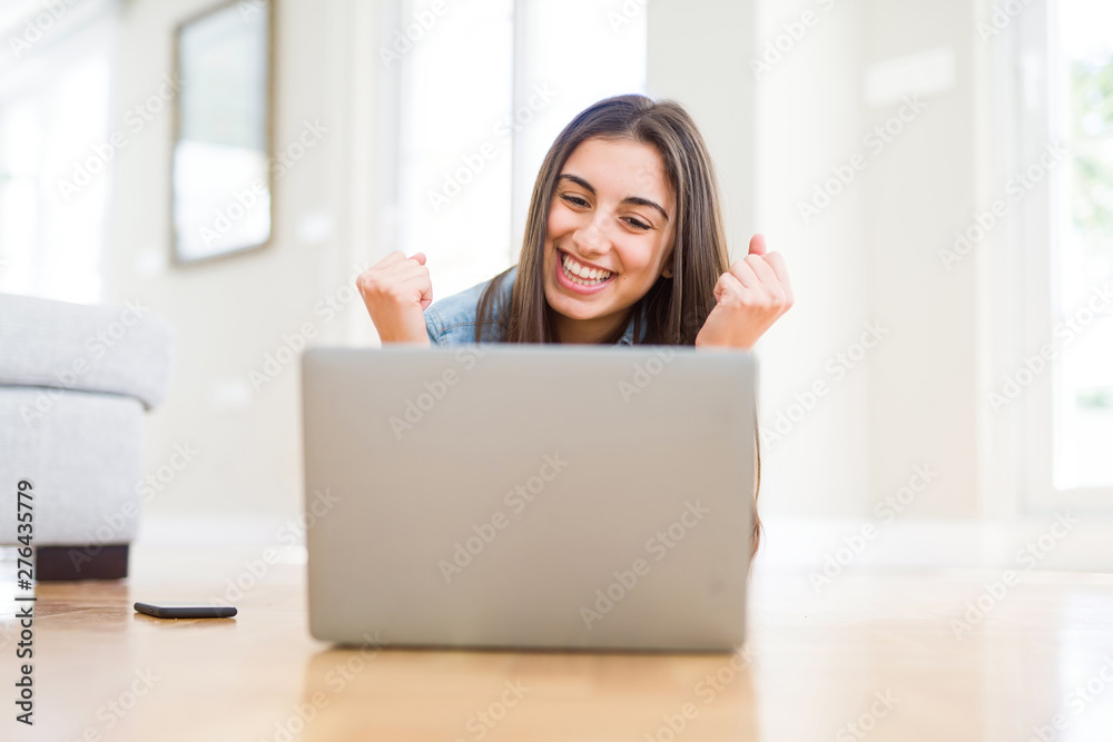 Beautiful young woman laying on the floor using laptop screaming proud and celebrating victory and success very excited, cheering emotion Beautiful young woman laying on the floor using laptop screaming proud and celebrating victory and success very excited, cheering emotion