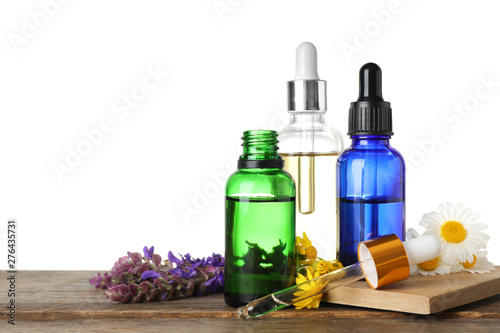 Bottles of different essential oils and wildflowers on wooden table  white background