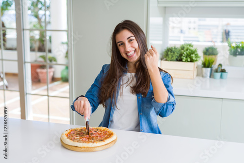 Fotografía Beautiful young woman cutting a tasty pizza slice using a cutter screaming proud