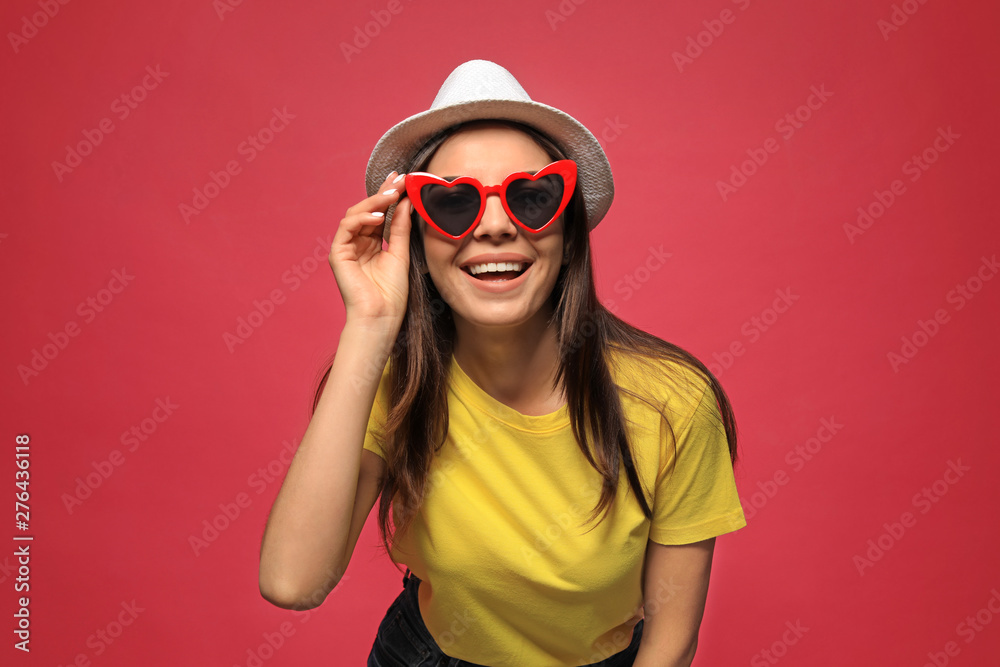Portrait of beautiful young woman with heart shaped sunglasses on color background