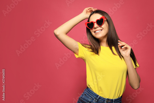 Portrait of beautiful young woman with heart shaped sunglasses on color background. Space for text