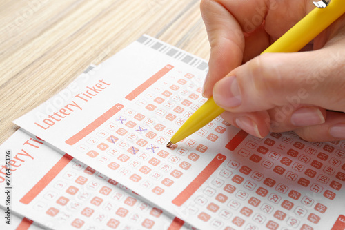 Woman filling out lottery tickets with pen on wooden table, closeup. Space for text