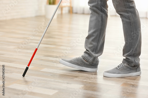 Blind person with long cane walking indoors, closeup