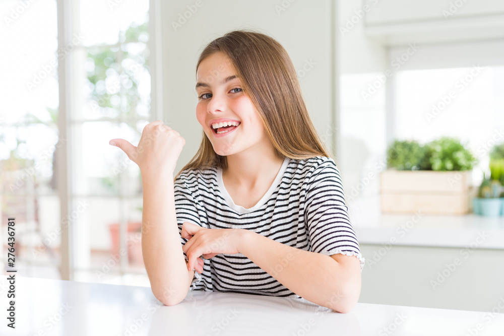 Beautiful young girl kid wearing stripes t-shirt smiling with happy face looking and pointing to the side with thumb up. Beautiful young girl kid wearing stripes t-shirt smiling with happy face looking and pointing to the side with thumb up.