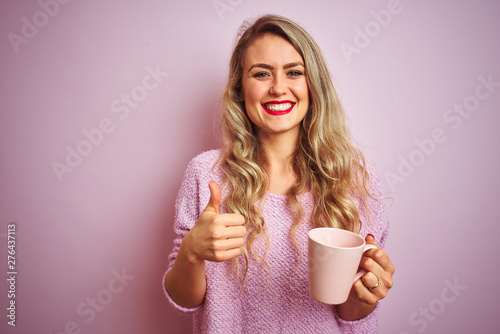 Young beautiful woman wearing sweater drinking a cup of coffee over pink isolated background happy with big smile doing ok sign, thumb up with fingers, excellent sign