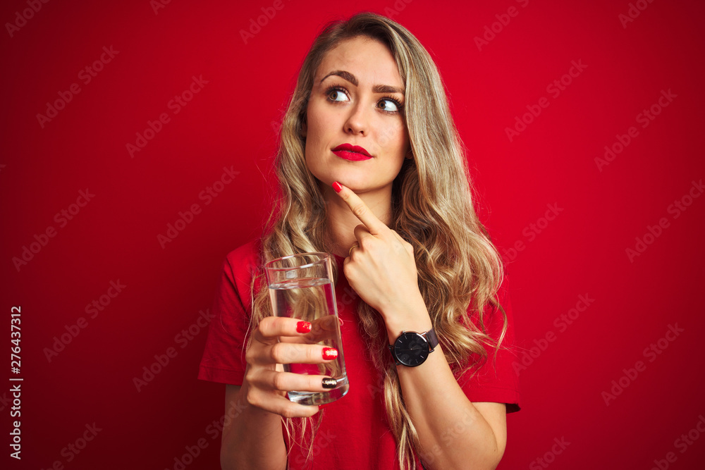 Young beautiful woman drinking a glass of water over red isolated background serious face thinking about question, very confused idea