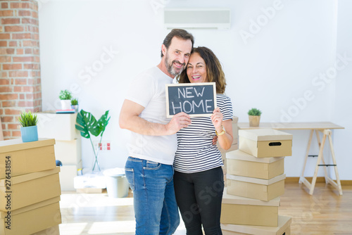 Middle age senior couple moving to a new house, smiling happy in love with apartmant holding a blackboard with new home text photo