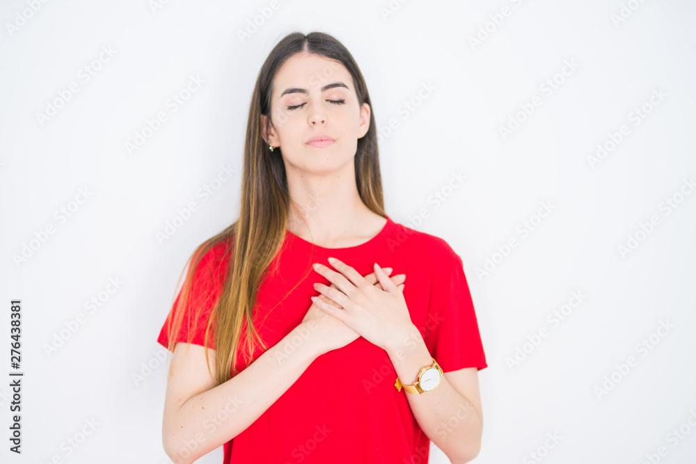 Young beautiful woman wearing casual red t-shirt over white isolated background smiling with hands on chest with closed eyes and grateful gesture on face. Health concept. Young beautiful woman wearing casual red t-shirt over white isolated background smiling with hands on chest with closed eyes and grateful gesture on face. Health concept.