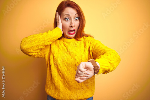 Beautiful redhead woman wearing winter sweater standing over isolated yellow background Looking at the watch time worried, afraid of getting late © Krakenimages.com