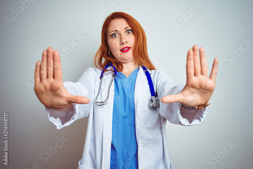 Young redhead doctor woman using stethoscope over white isolated background doing stop gesture with hands palms  angry and frustration expression
