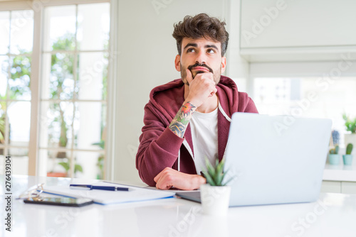 Young student man using computer laptop and notebook serious face thinking about question, very confused idea