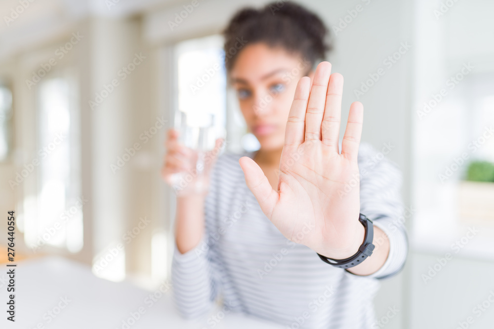 Young african american girl drinking a fresh glass of water with open hand doing stop sign with serious and confident expression, defense gesture Young african american girl drinking a fresh glass of water with open hand doing stop sign with serious and confident expression, defense gesture