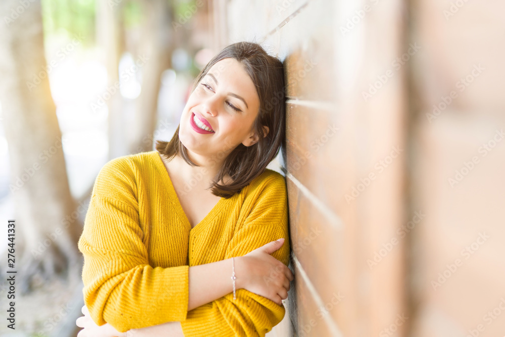 Beautiful young woman smiling confident and cheerful leaning on wooden wall, walking on the street of the city on a sunny day Beautiful young woman smiling confident and cheerful leaning on wooden wall, walking on the street of the city on a sunny day
