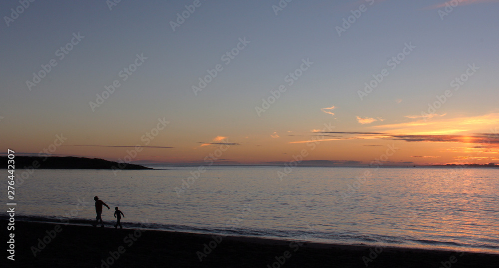Sunset at ocean with silhouette of man and boy walking along beach with copy space
