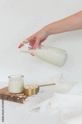 Woman's Hand Pouring Oat Milk into A Clear Glass, White Background, Copy Space